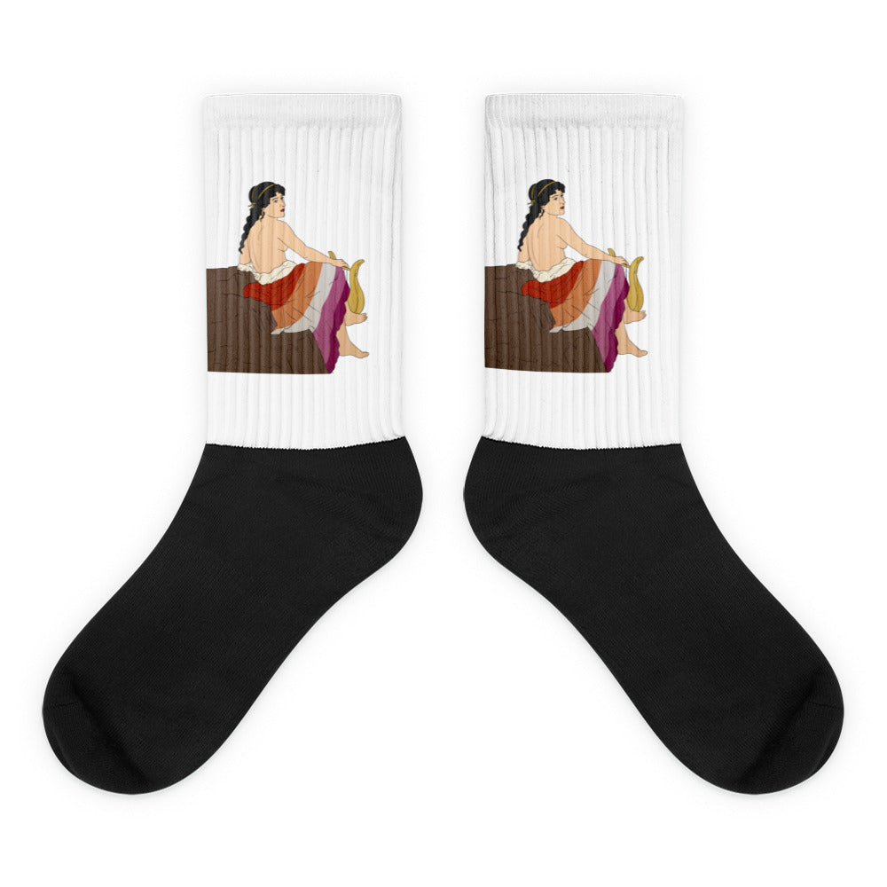 Pair of crew socks with black feet and white cuffs showing a seated classical woman with a vase