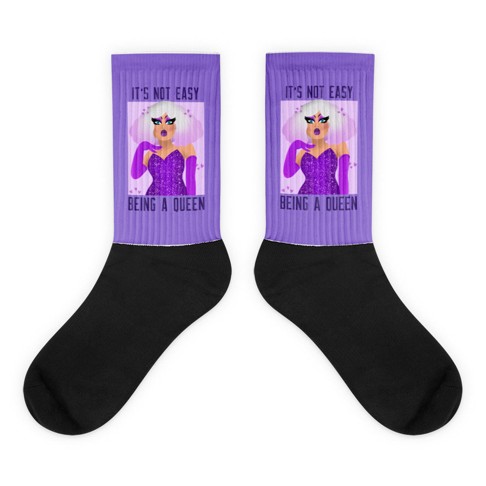 Pair of black-and-purple socks showing a glamorous illustrated queen and “IT’S NOT EASY BEING A QUEEN”
