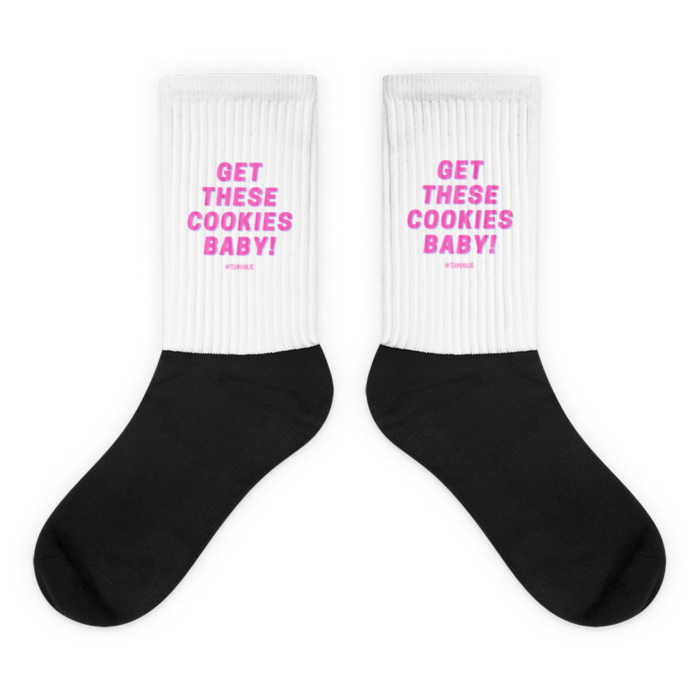 Pair of white-and-black crew socks reading “GET THESE COOKIES BABY!” in pink