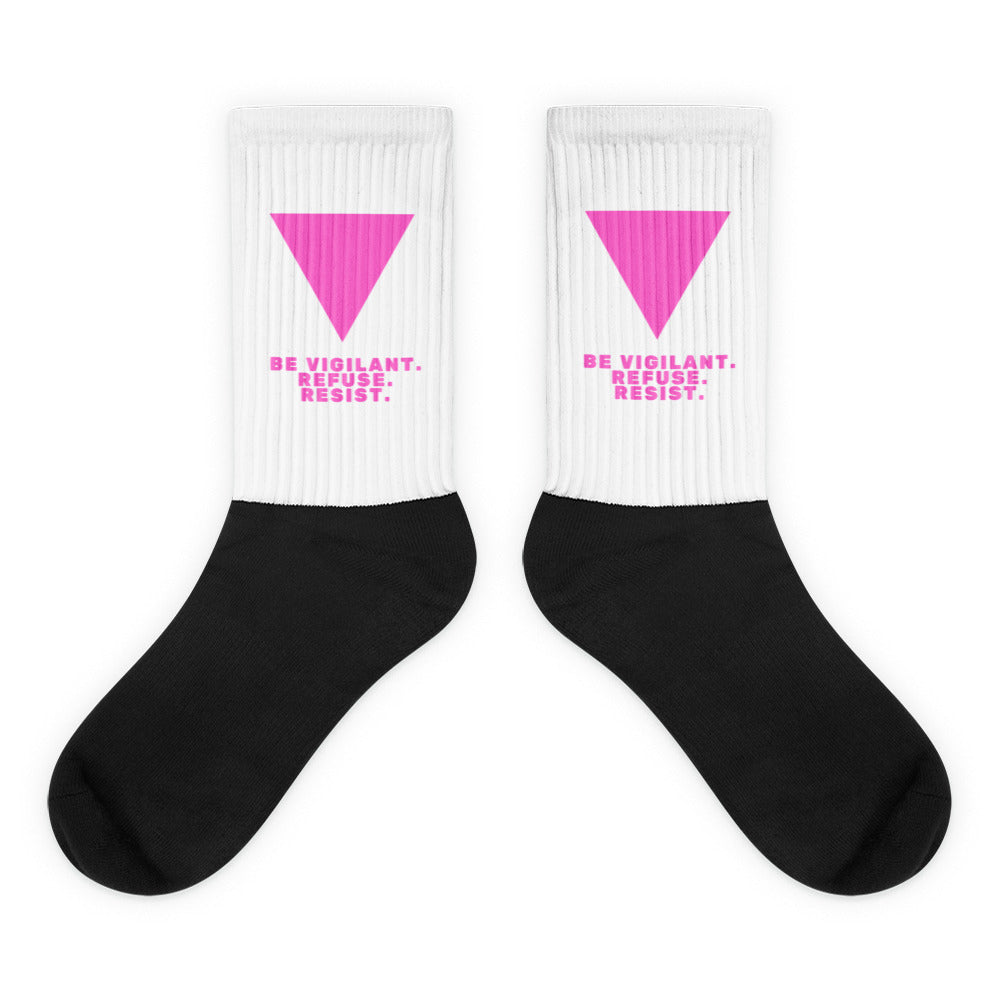 Pair of black-and-white ribbed socks with pink triangles and “BE VIGILANT. REFUSE. RESIST.” text