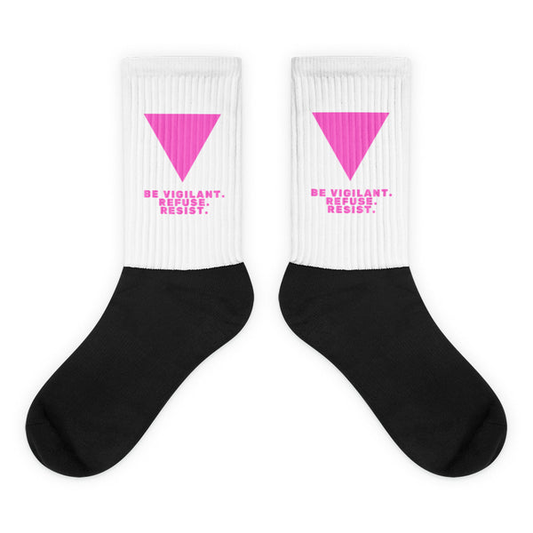 Pair of black-and-white ribbed socks with pink triangles and “BE VIGILANT. REFUSE. RESIST.” text
