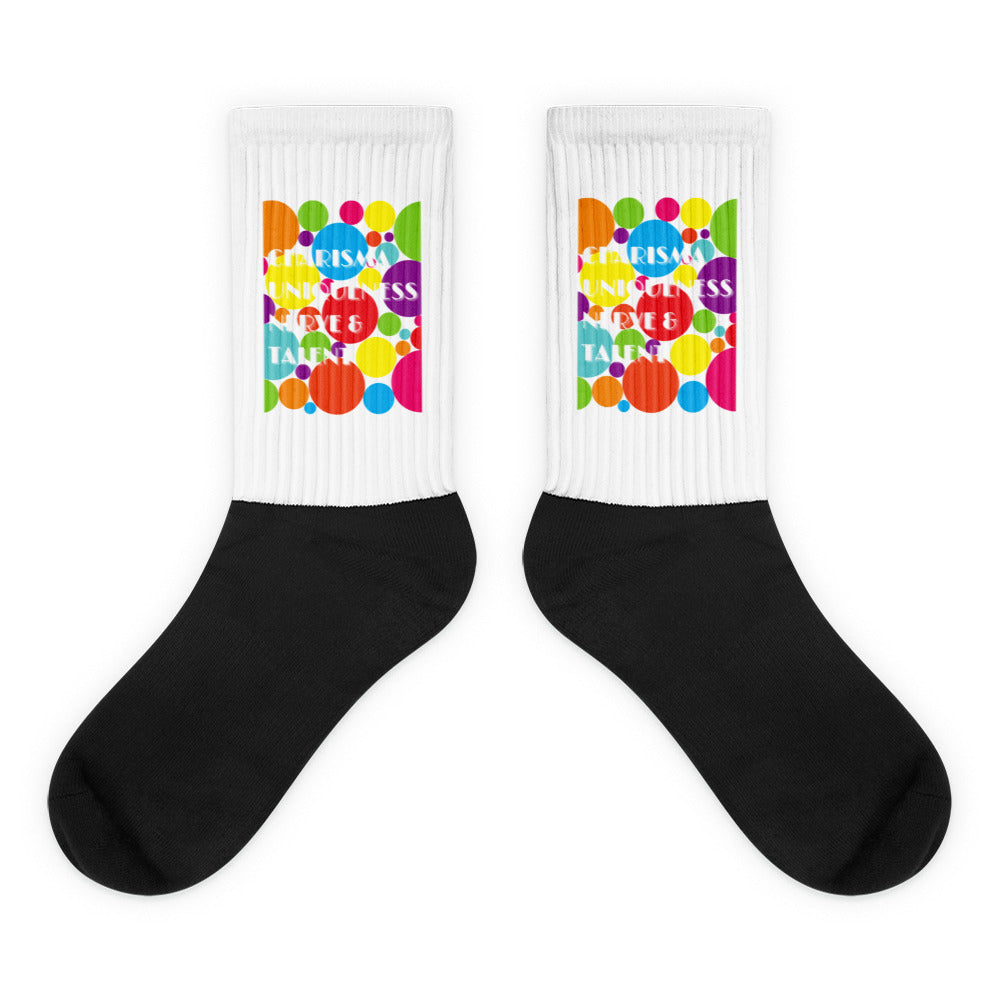 Pair of black-and-white socks with colorful dots and “CHARISMA, UNIQUENESS, NERVE & TALENT” text