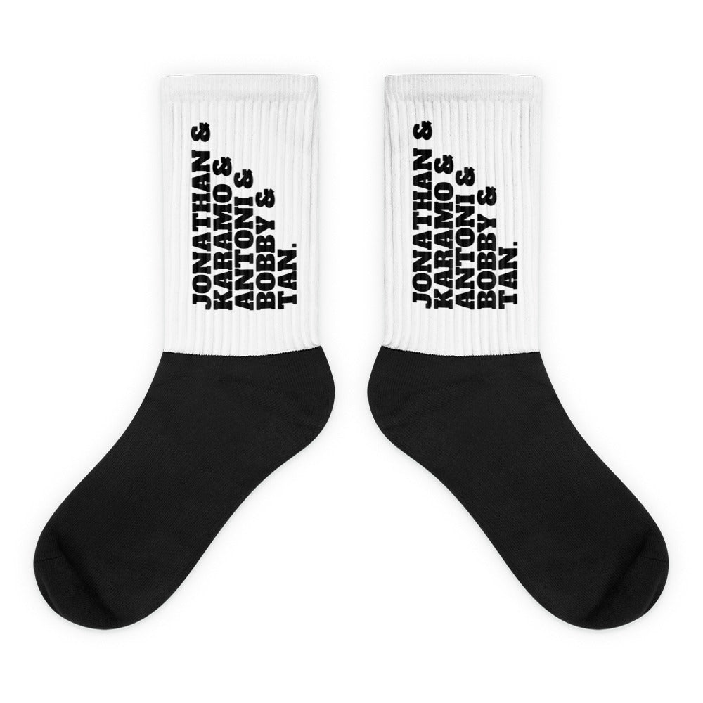 Pair of white ribbed socks with black feet and stacked names Jonathan, Karamo, Antoni, Bobby, and Tan