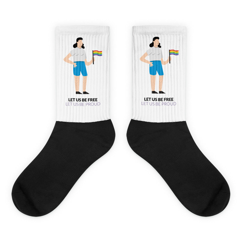 Pair of white-and-black socks with a person holding a rainbow flag and “LET US BE FREE” text