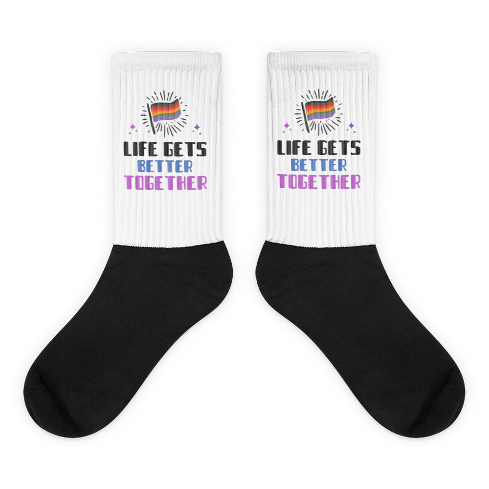 Pair of white-and-black crew socks reading “LIFE GETS BETTER TOGETHER” with rainbow flags