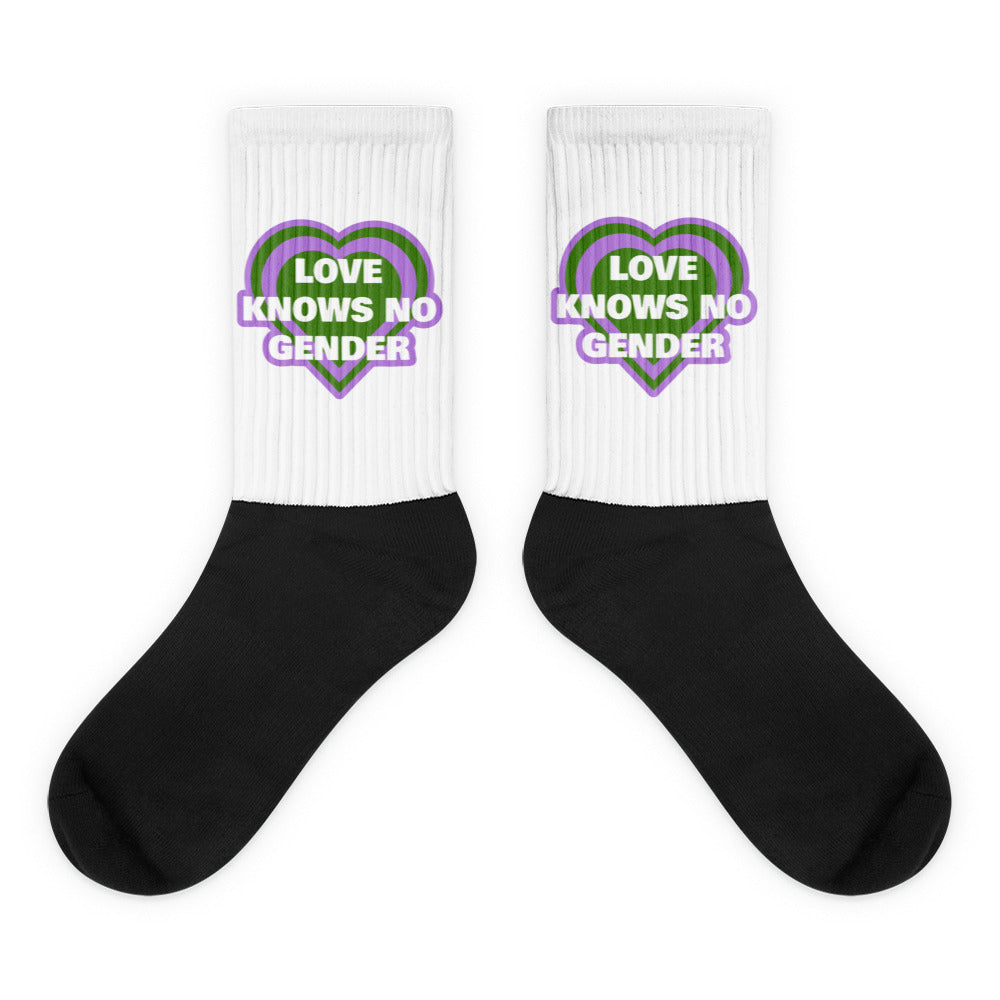 Pair of crew socks with black feet, white ribbed cuffs, and heart slogan reading “LOVE KNOWS NO GENDER.”