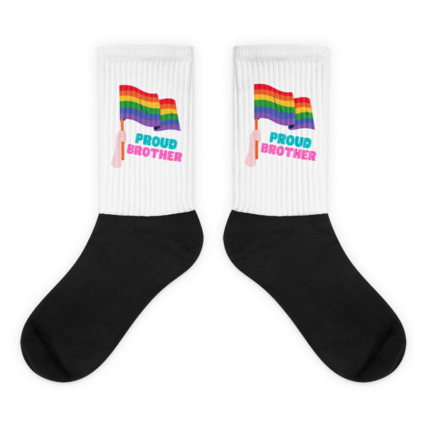 Proud Brother Socks feature a black foot and a white leg with a graphic of a hand holding a rainbow pride flag and PROUD BROTHER in colorful letters, celebrating queer pride and visibility.