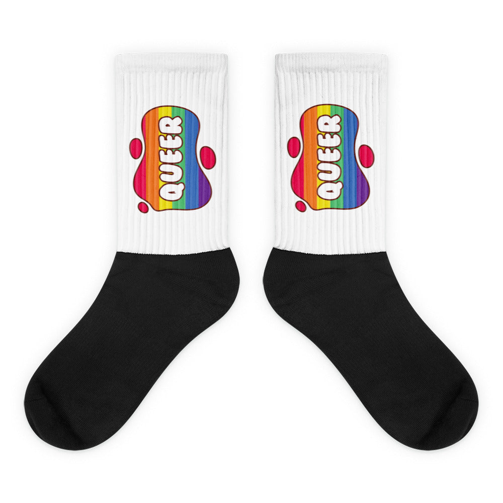 Pair of crew socks with black feet and white ribbed cuffs bearing rainbow QUEER graphics