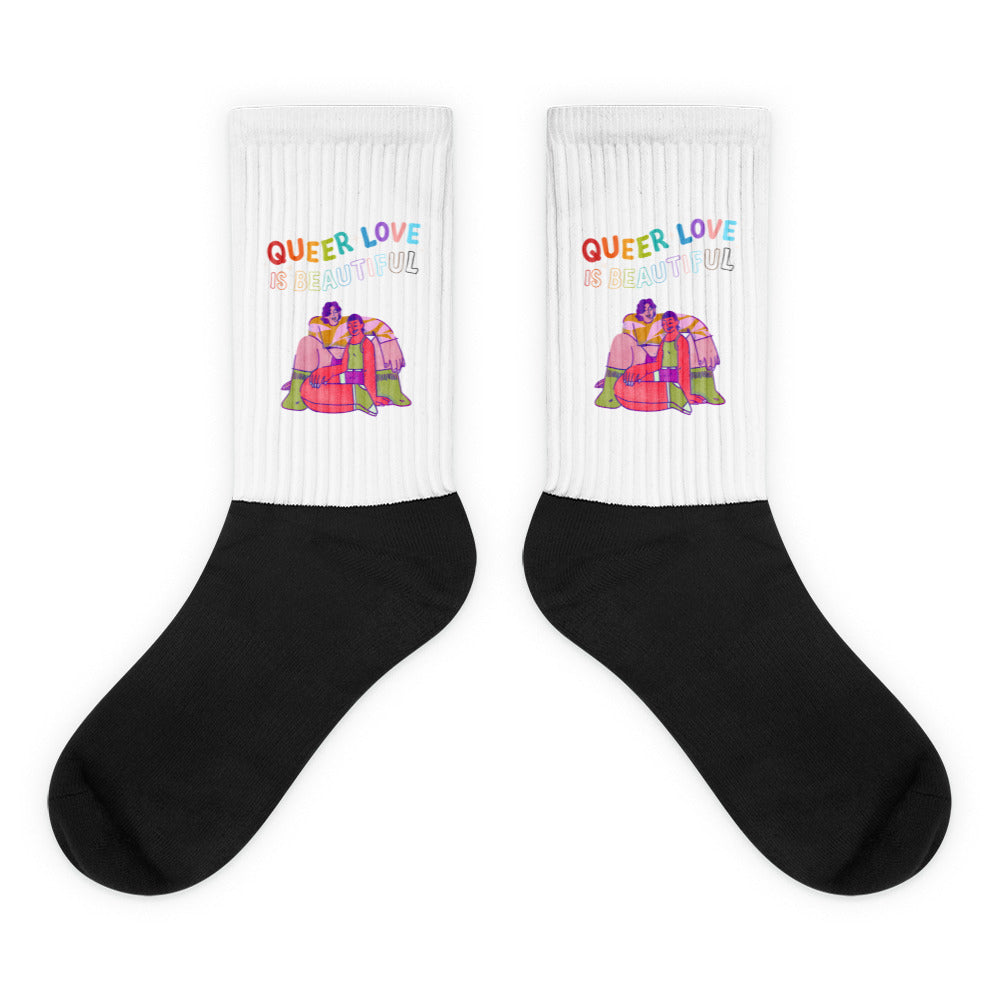 Pair of black-and-white socks reading “QUEER LOVE IS BEAUTIFUL,” with colorful embracing figures