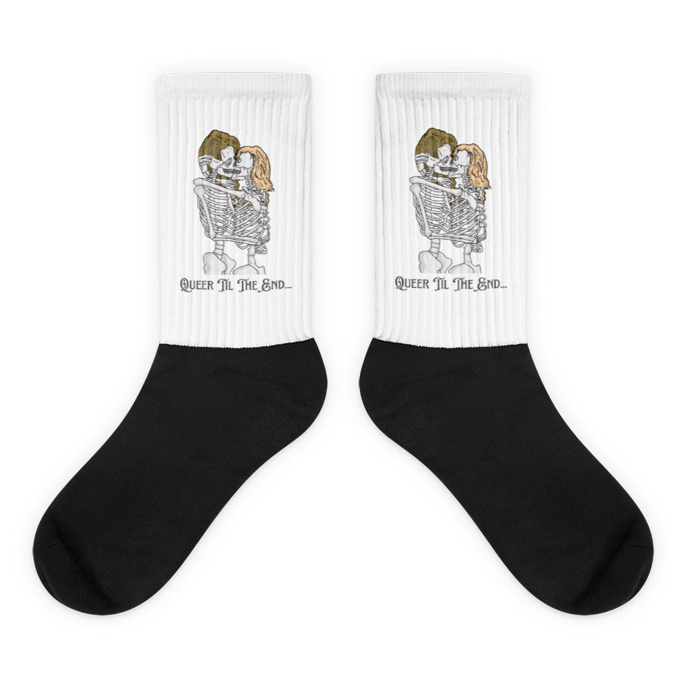 Pair of black-and-white socks showing embracing skeletons and “Queer Til The End...” text