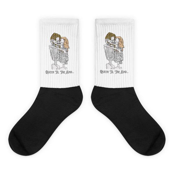 Pair of black-and-white socks showing embracing skeletons and “Queer Til The End...” text