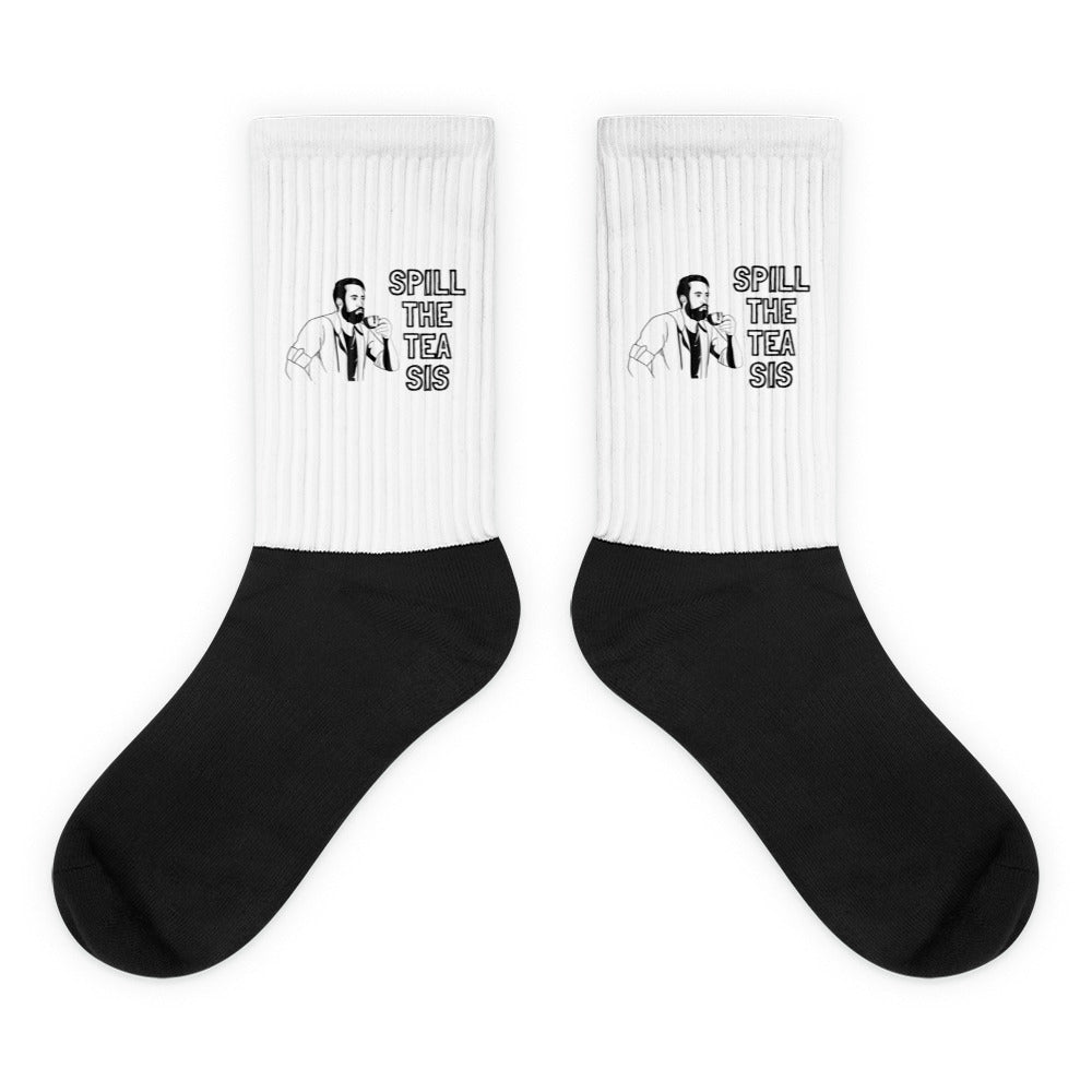 Pair of black-and-white crew socks reading “SPILL THE TEA SIS” with a bearded figure
