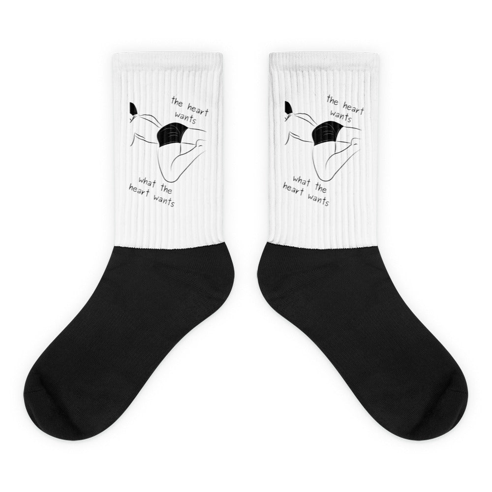 Pair of black-and-white socks with a reclining figure and “the heart wants what the heart wants” text