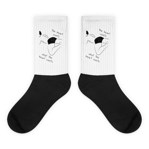 Pair of black-and-white socks with a reclining figure and “the heart wants what the heart wants” text
