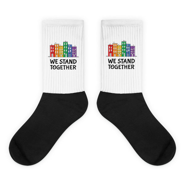 We Stand Together Socks: Crew-length socks with black foot and white leg, featuring rainbow cityscapes and WE STAND TOGETHER. Crafted in a nylon-cotton-spandex blend, embodying vibrant queer pride and empowerment.