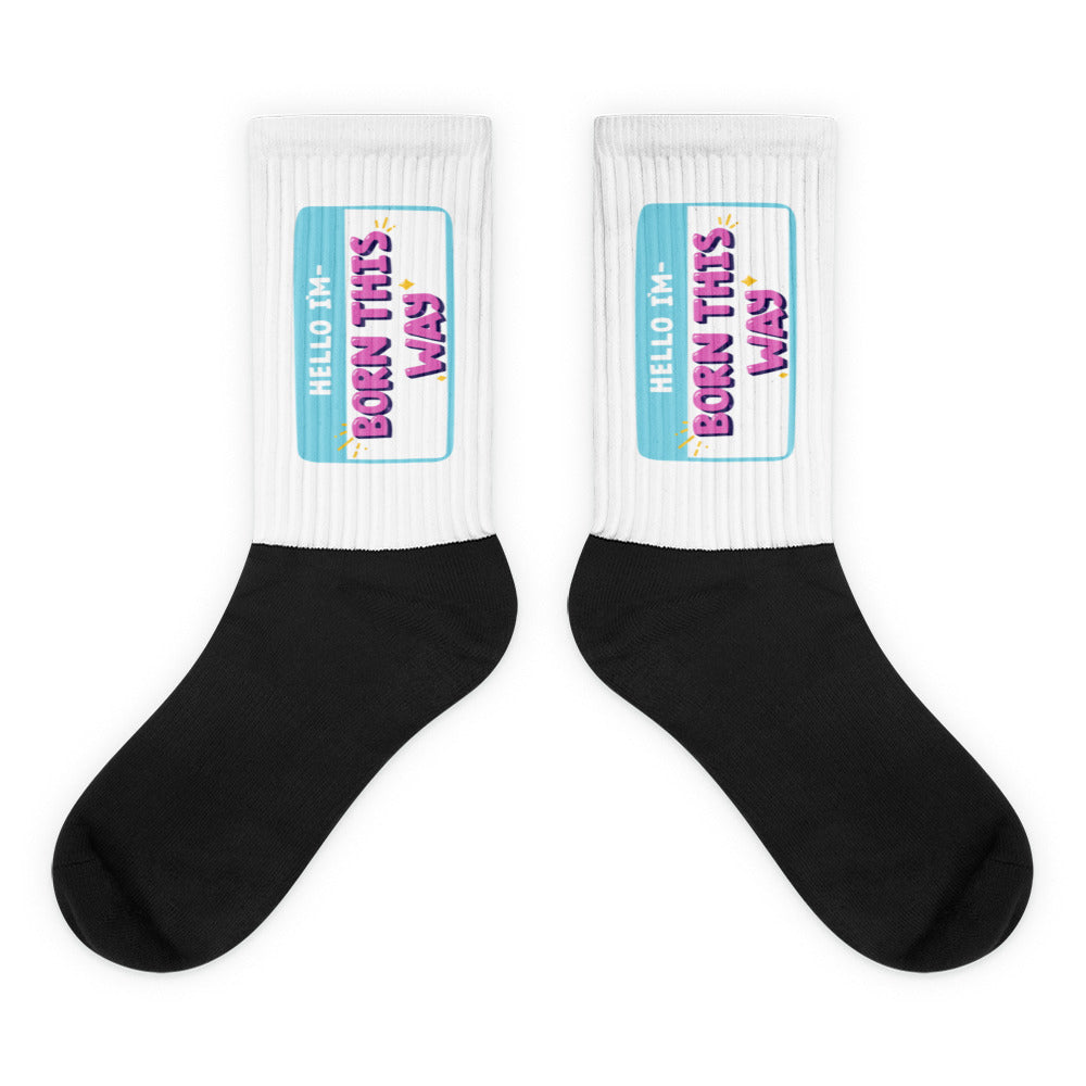 Pair of black-and-white crew socks with turquoise labels reading “HELLO I'M BORN THIS WAY”