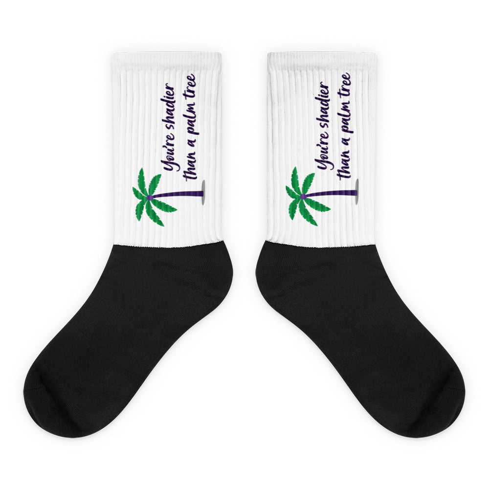 Pair of black-and-white socks with palm trees and “You’re shadier than a palm tree” text