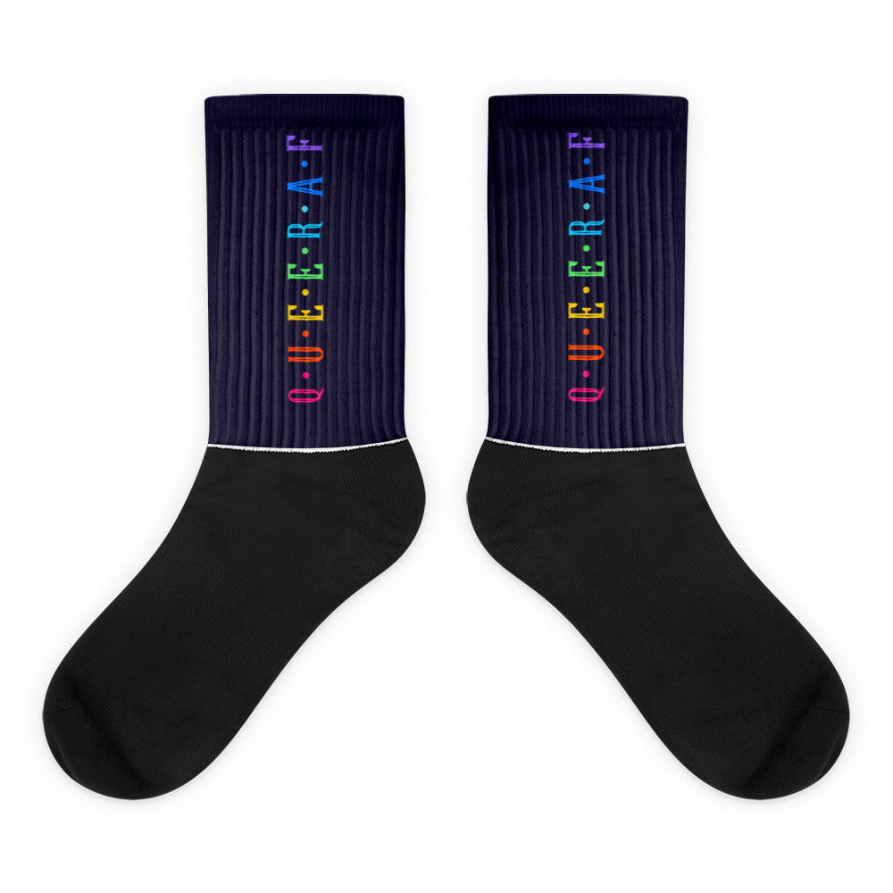 Pair of black socks with navy ribbed cuffs reading “QUEER AF” in rainbow letters