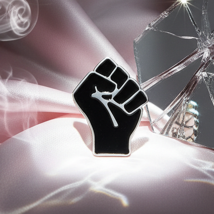 Black raised-fist enamel pin displayed against reflective shattered glass