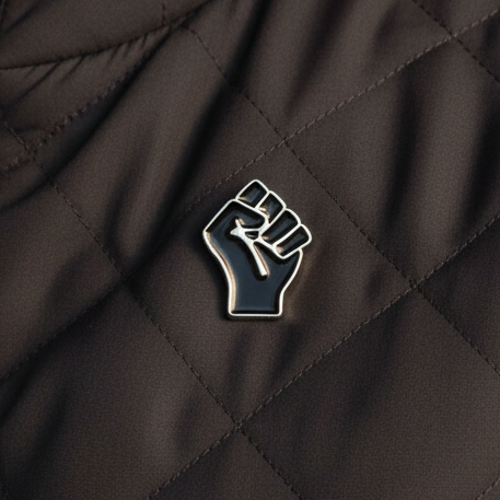 Black raised-fist enamel pin on quilted black fabric
