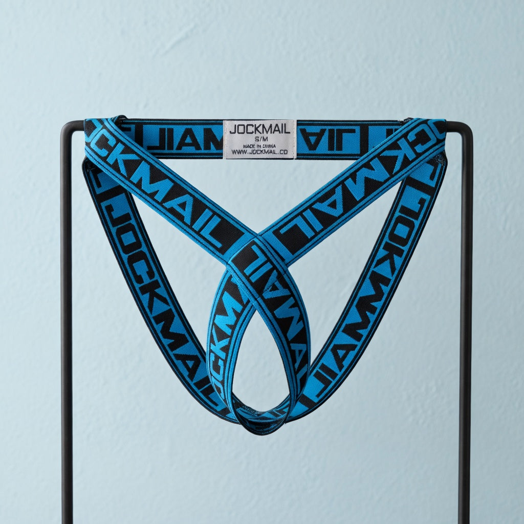Blue and black Jockmail elastic cockstrap displayed unworn on a black frame against pale blue plaster.