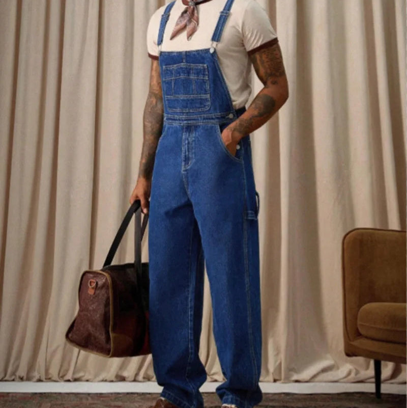 Model wearing blue denim overalls over a white T-shirt, holding a brown duffel bag