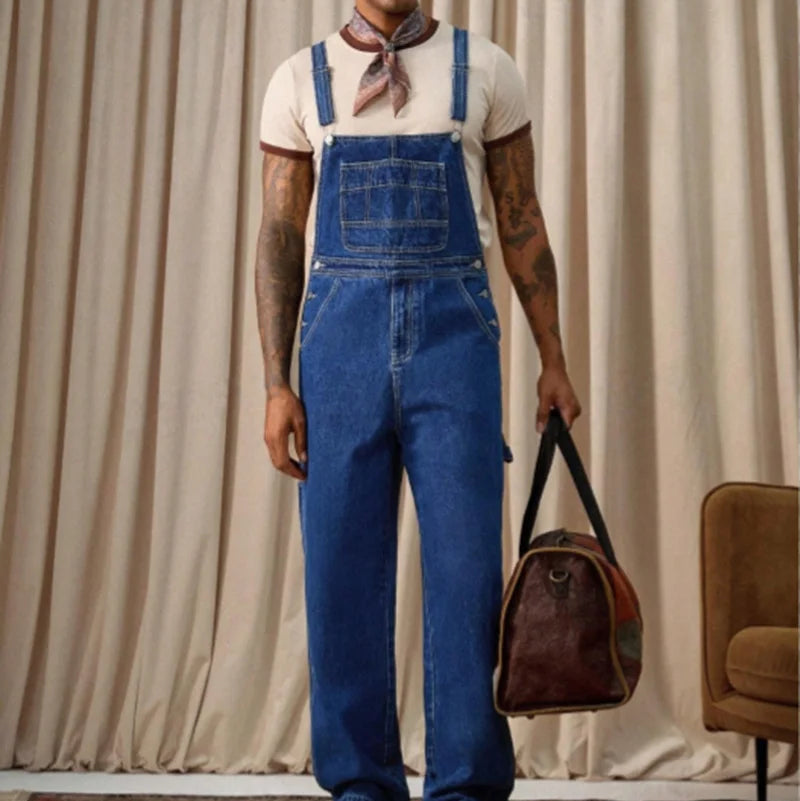 Front view of a person wearing blue denim overalls over a white shirt and holding a brown bag