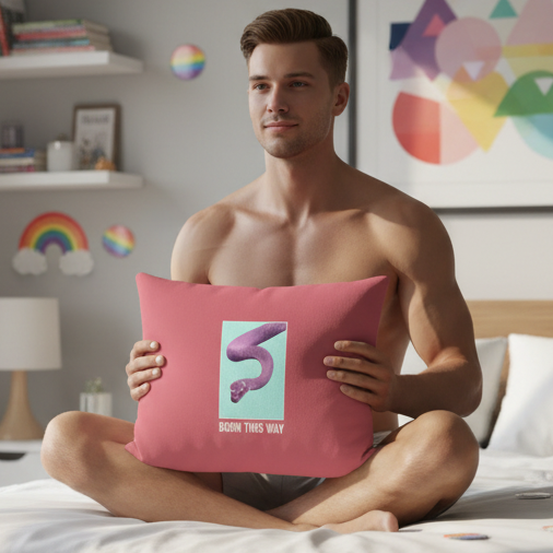 Shirtless person sits cross-legged on bed, holding "Born This Way" pillow with purple snake and LGBT message in