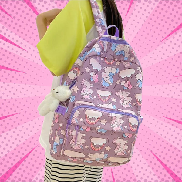 Unicorn-print backpack worn on a model, with a front zip pocket and plush bunny charm