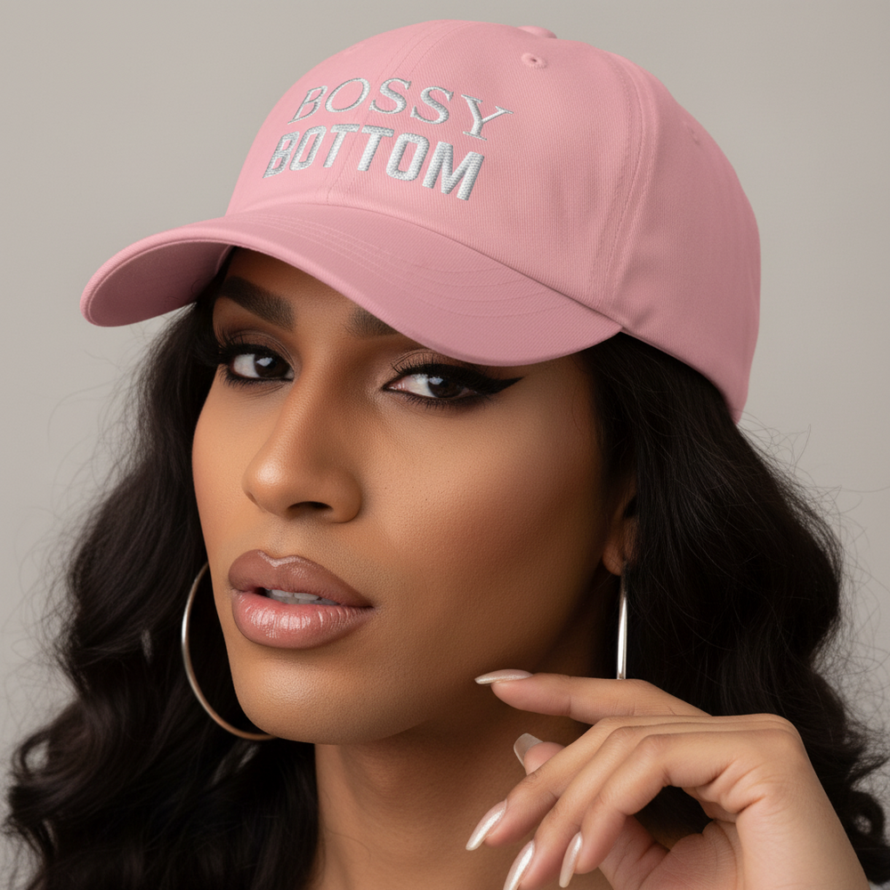 Bossy Bottom Cap, a pink pride hat with “BOSSY BOTTOM” embroidery, worn by someone with long dark hair, hoops