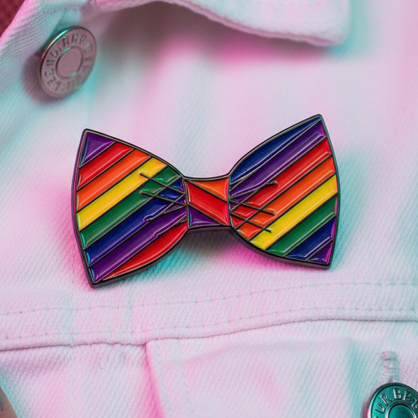 Rainbow-striped bow tie enamel pin on a pale pink garment