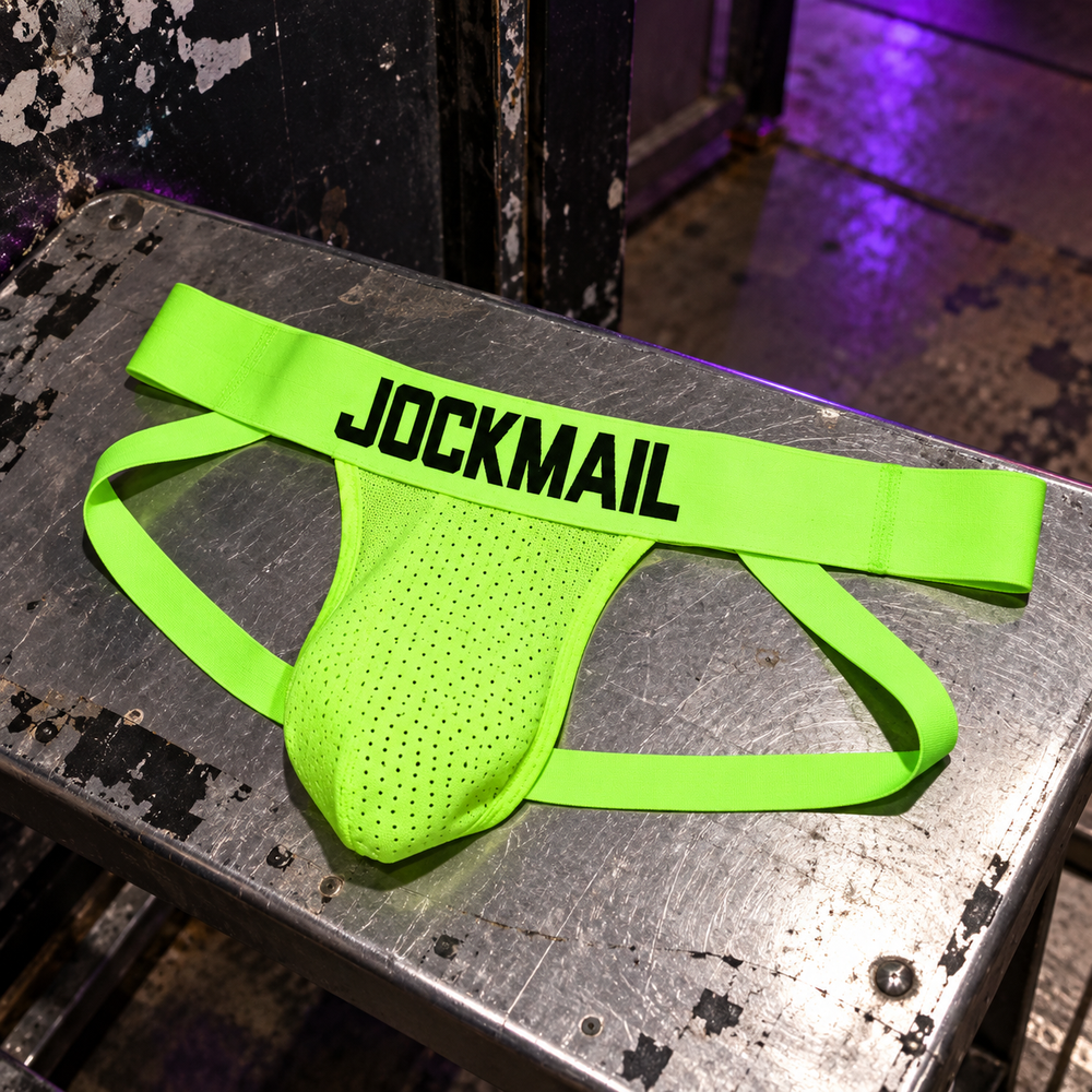 Jockmail Neon Party Jockstrap in Green, photographed at a low steel bench inside a scuffed warehouse venue entrance.