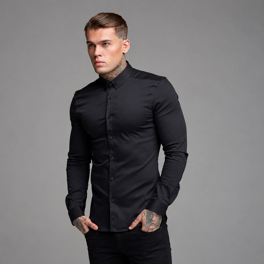 Front three-quarter view of a tattooed person wearing a fitted black long-sleeve button-up shirt
