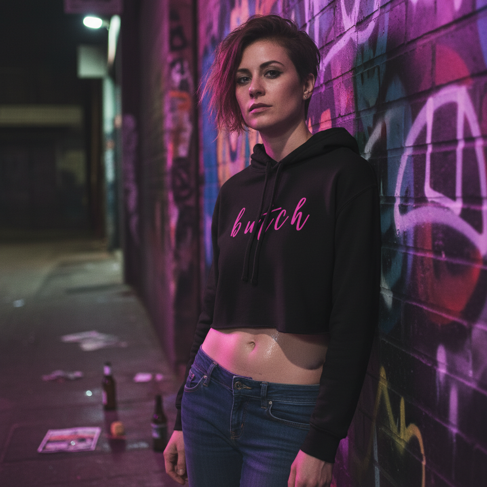 Butch Crop Hoodie on a short-haired person posing at night by a graffiti wall, lit by pink and purple lights