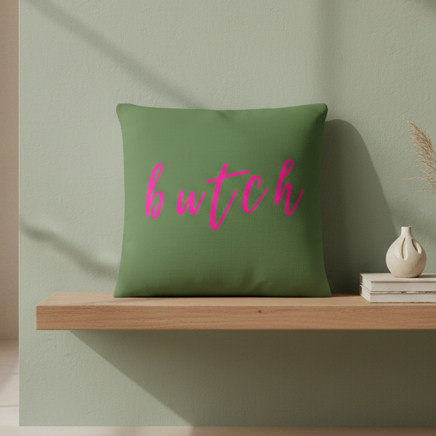 Green "Butch Pillow" with “butch” in bold pink cursive on a wooden shelf