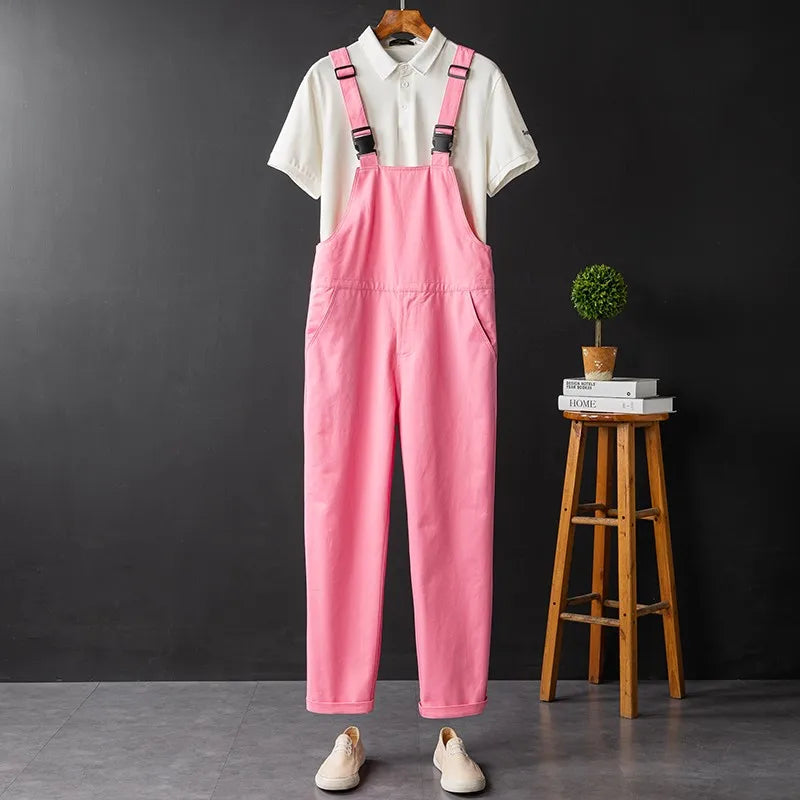 Pink bib overalls with black buckles over a white polo shirt, displayed with sneakers