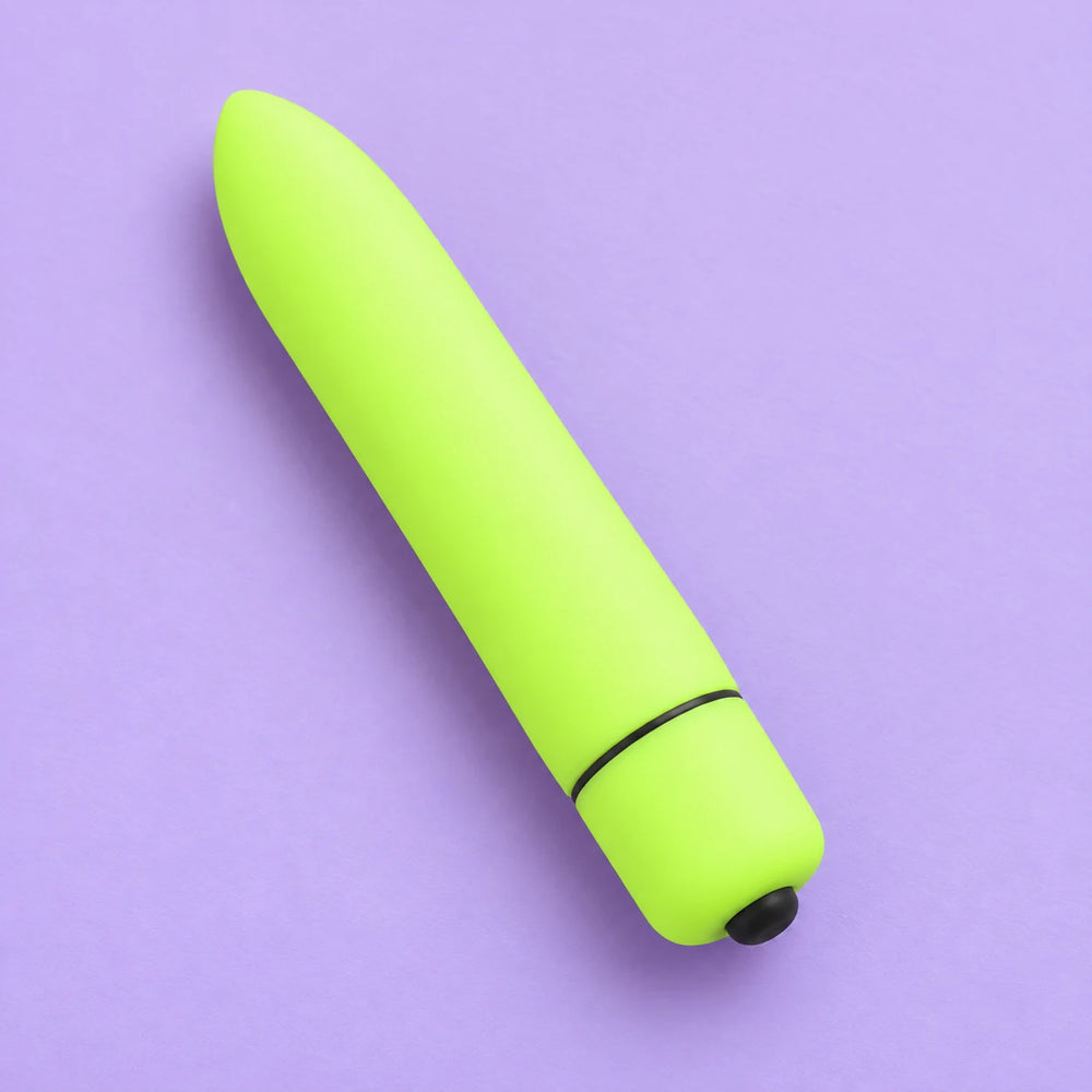 Neon-green mini bullet vibrator lying diagonally on lavender, showing its tapered tip, base seam and black button.