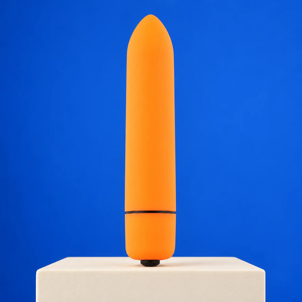 Orange mini bullet vibrator with a black base button and cap seam standing on an ivory block against cobalt blue.