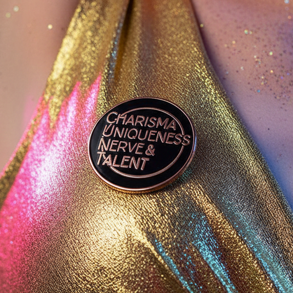Close-up of black enamel pin reading “CHARISMA UNIQUENESS NERVE & TALENT” on shimmering fabric