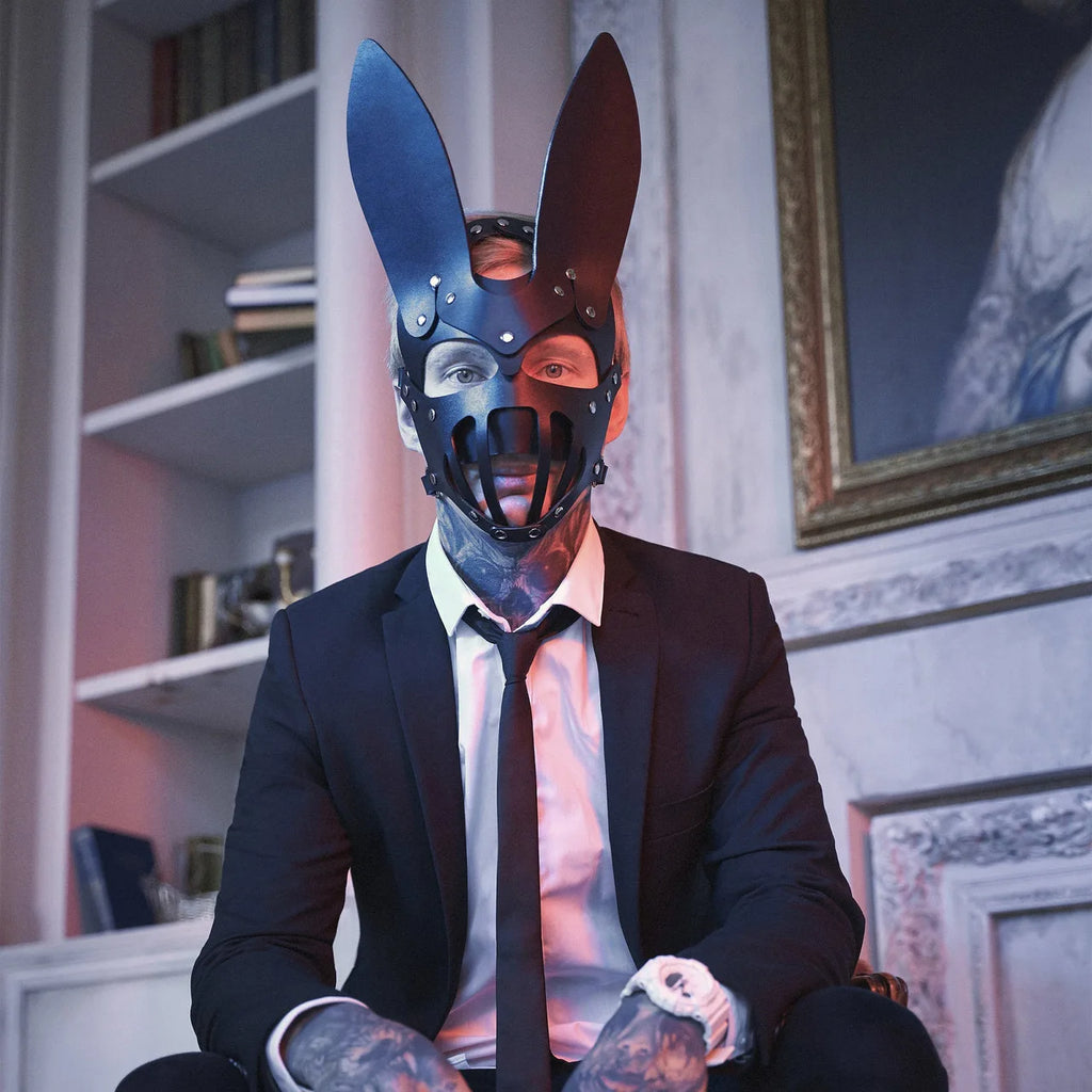 Person in a suit wearing a black bunny mask with tall ears, studs, and mouth bars