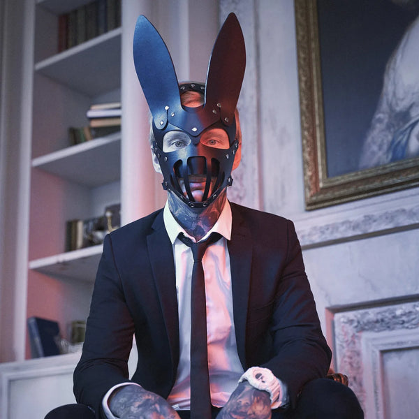 Person in a suit wearing a black bunny mask with tall ears, studs, and mouth bars