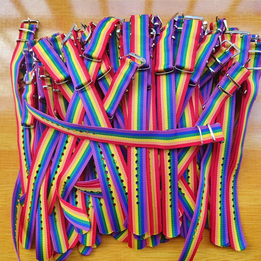 Pile of rainbow-striped adjustable fabric Pride bracelets with silver buckles on a wooden surface