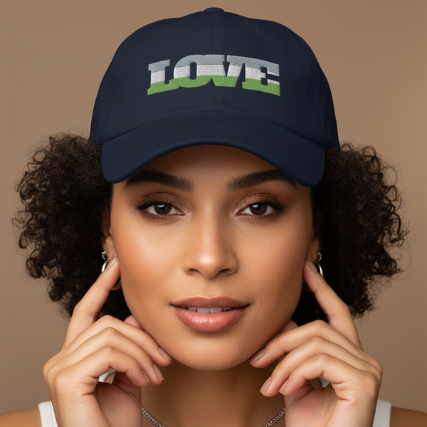 Genderqueer Love Cap: a navy pride hat repping “LOVE” in bold white and green, rocked by a curly-haired femme against beige.