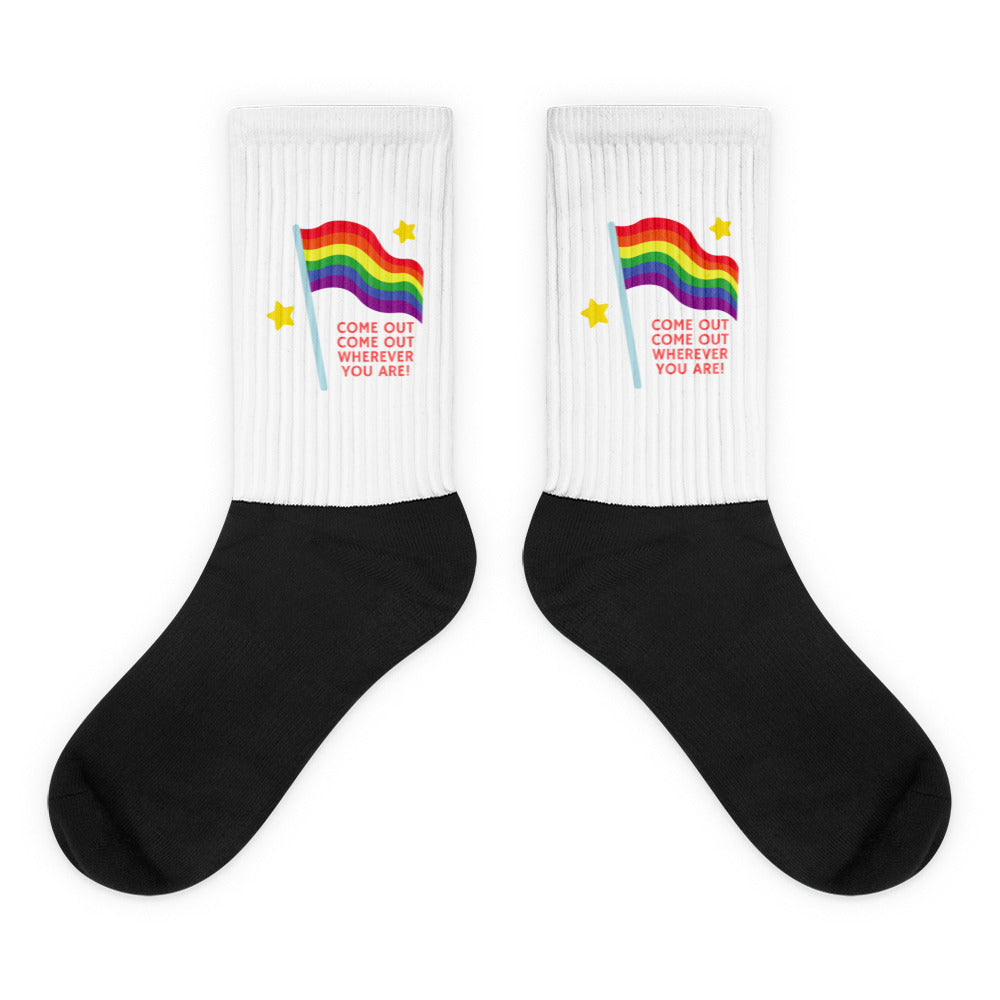 Pair of black-and-white socks with rainbow flags, yellow stars, and red “COME OUT” text