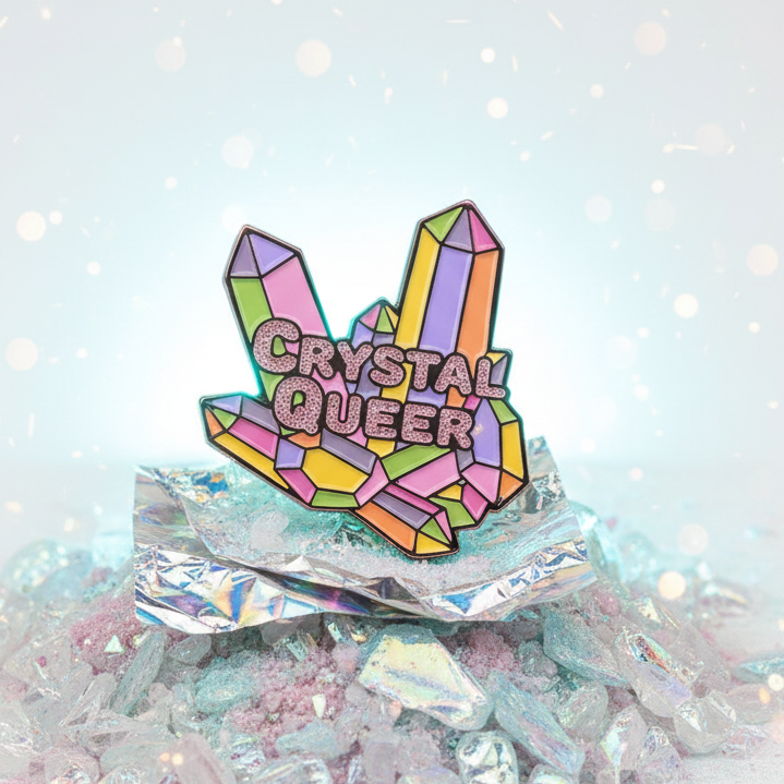 Close-up of a colorful crystal-shaped enamel pin reading “CRYSTAL QUEER”