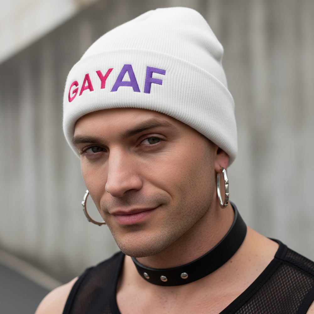 Gay AF Cuffed Beanie with vibrant rainbow letters worn by a light-skinned person in hoop earrings, mesh top, and choker.
