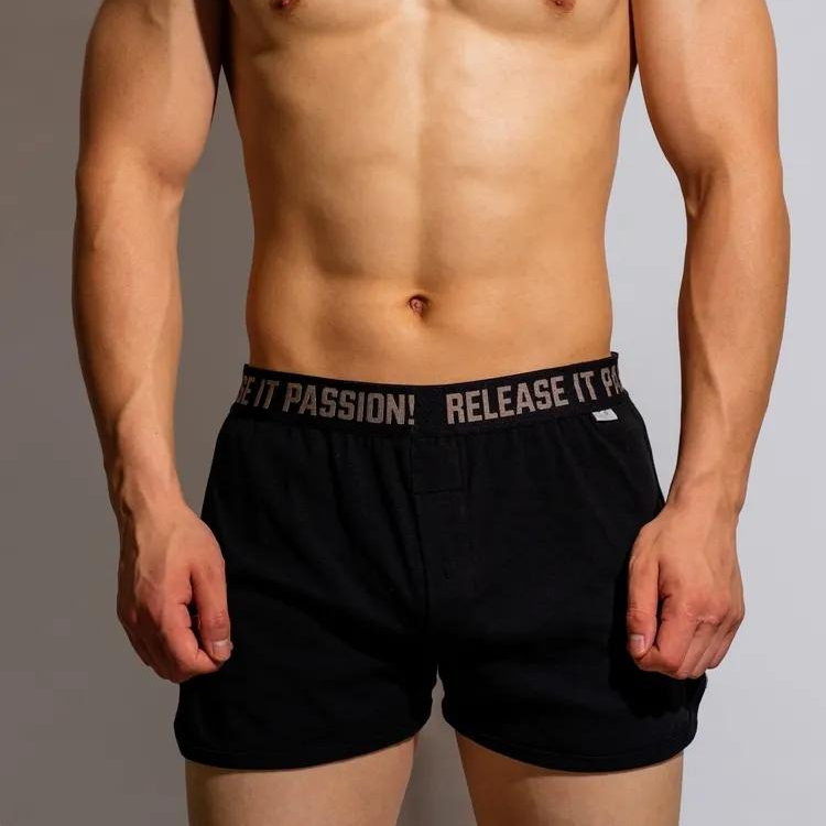 Front view of a shirtless model wearing black boxer shorts with a printed waistband