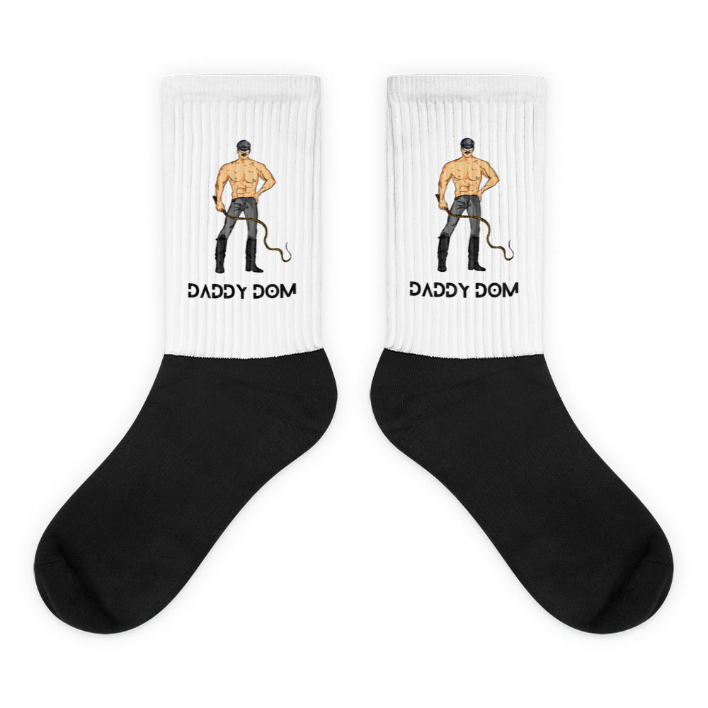 Pair of black-and-white crew socks showing a shirtless man with a whip and “DADDY DOM” text
