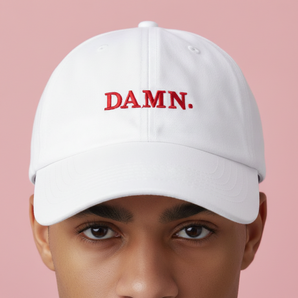 Model wearing a white baseball cap embroidered with red “DAMN.” lettering