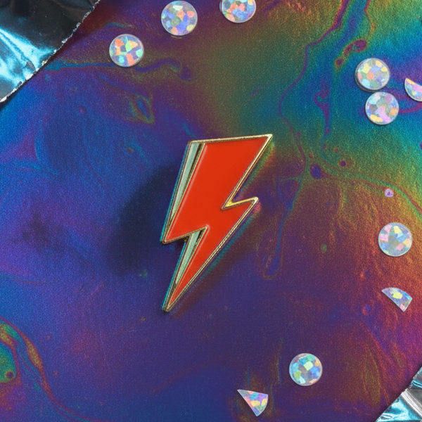 Red lightning bolt enamel pin on an iridescent purple-blue background